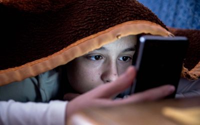 Dreng dækket af sin dyne kigger på sin mobil