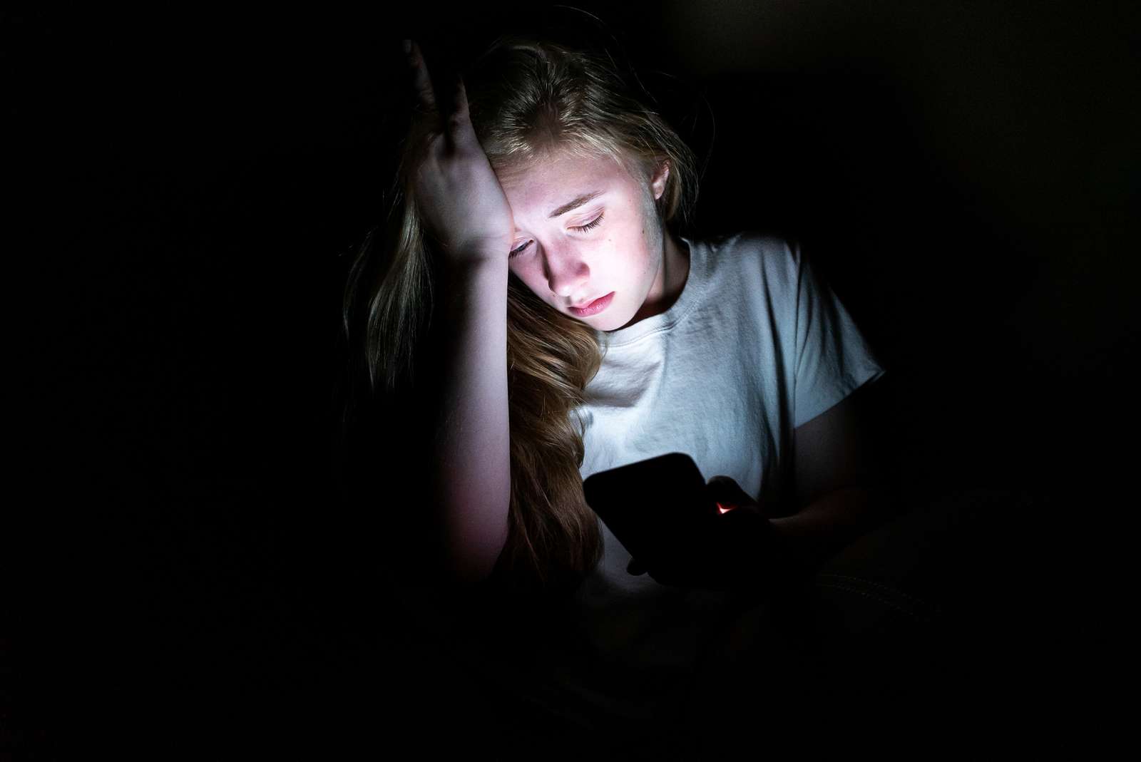 Trist pige holder hånden til hovedet mens hun kigger på sin mobil