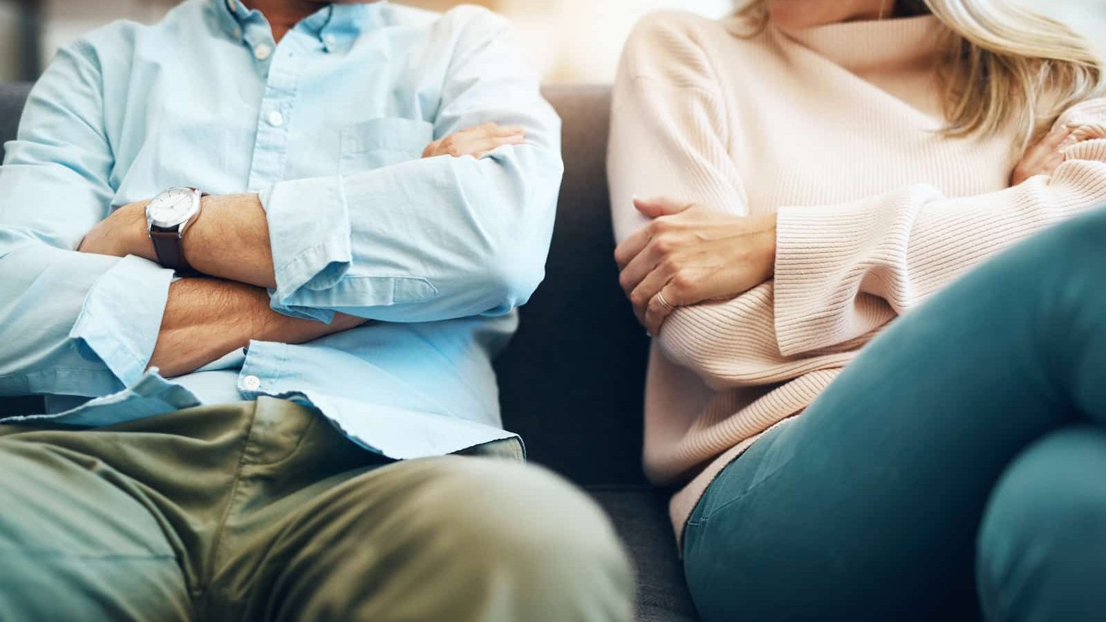 Mand og kvindes med hovedet skåret ud af billede sidder med krydsede arme på en sofa.
