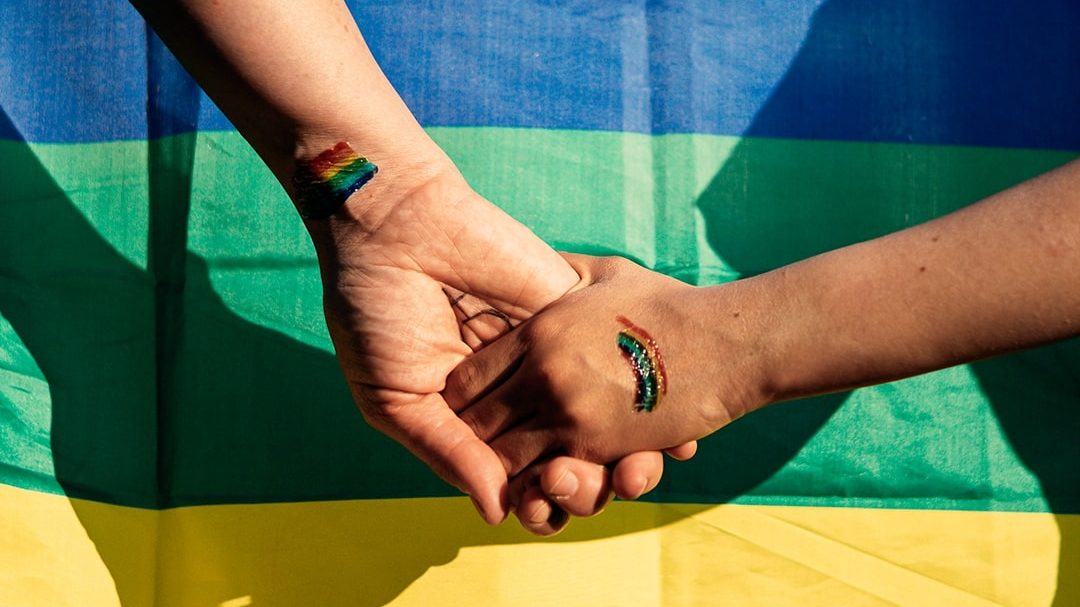 To hænder med regnbuer malet på holder i hånd foran et flag