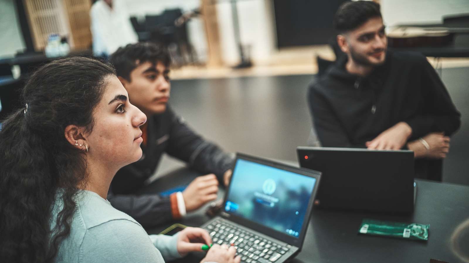 Tre unge sidder omkring et bord med deres laptops