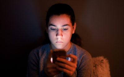 Mørkhåret dreng på mørk baggrund kigger ind i sin telefon