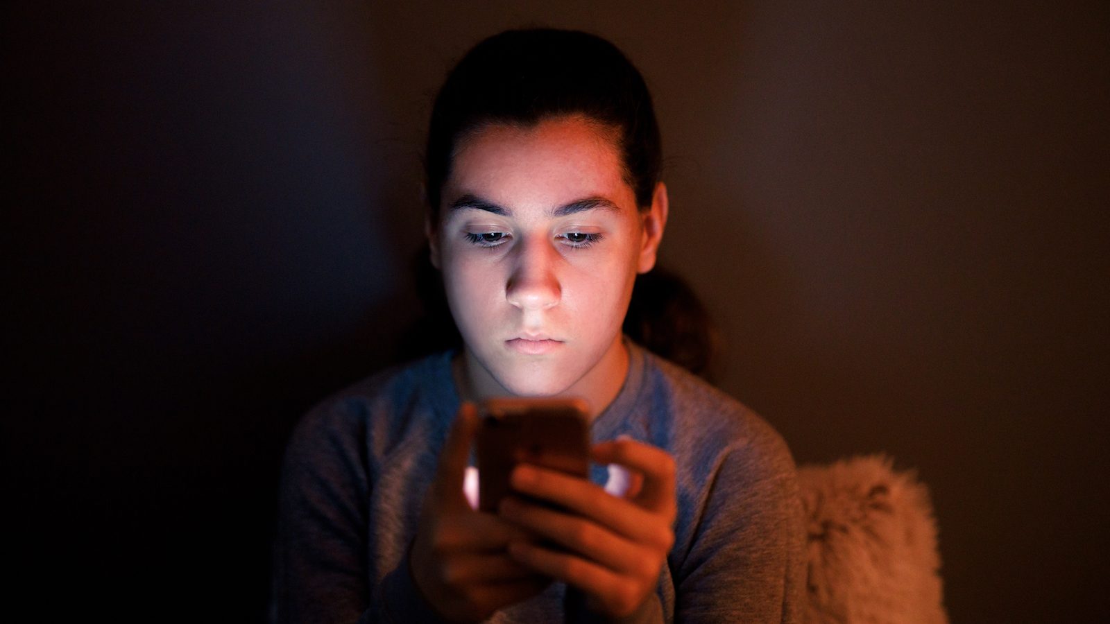 Mørkhåret dreng på mørk baggrund kigger ind i sin telefon