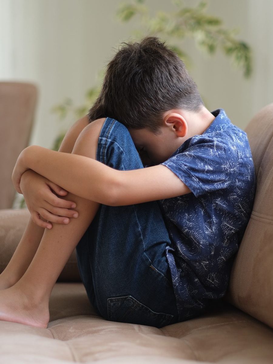 Dreng sidder på sofa med hovedet i knæene