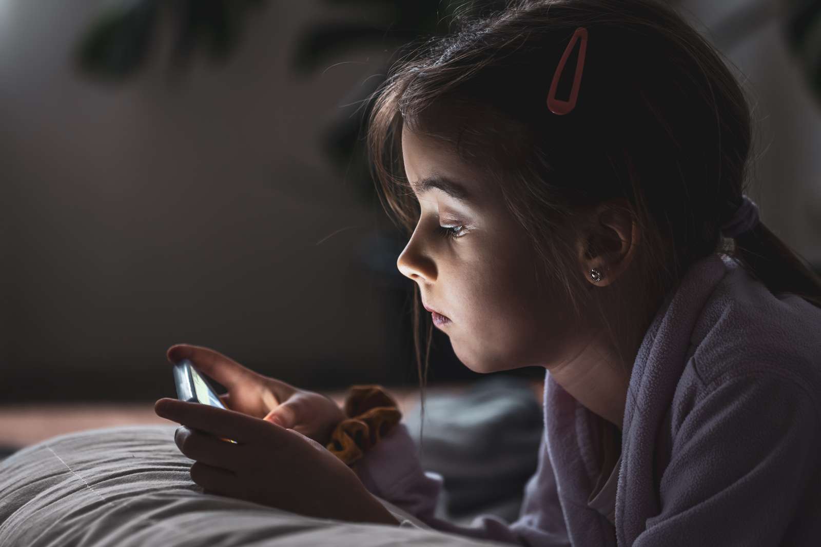 Brunhåret pige ligger på en seng, og kigger på en telefon.