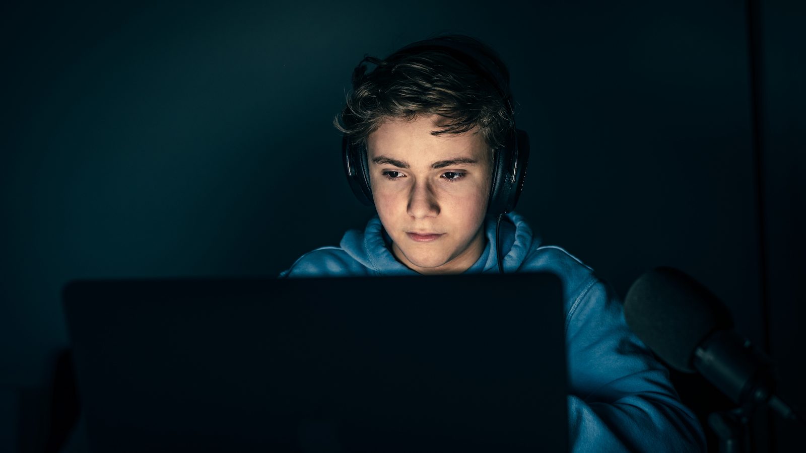 En dreng med headset på sidder og kigger på en computer.