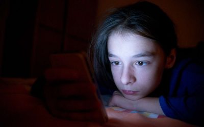 Pige ligger i mørke og kigger på sin telefon