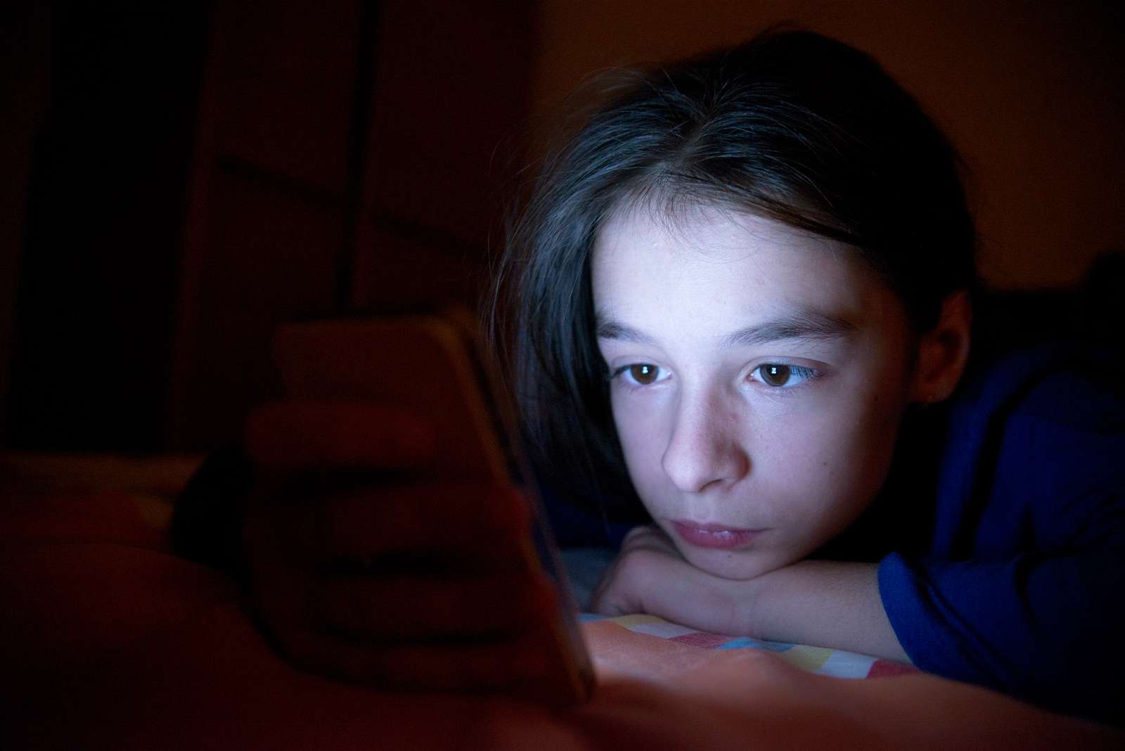 Pige ligger i mørke og kigger på sin telefon
