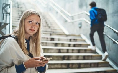 Blond pige for enden af en trappe, med sin telefon i hånden, kigger ind i kameraet