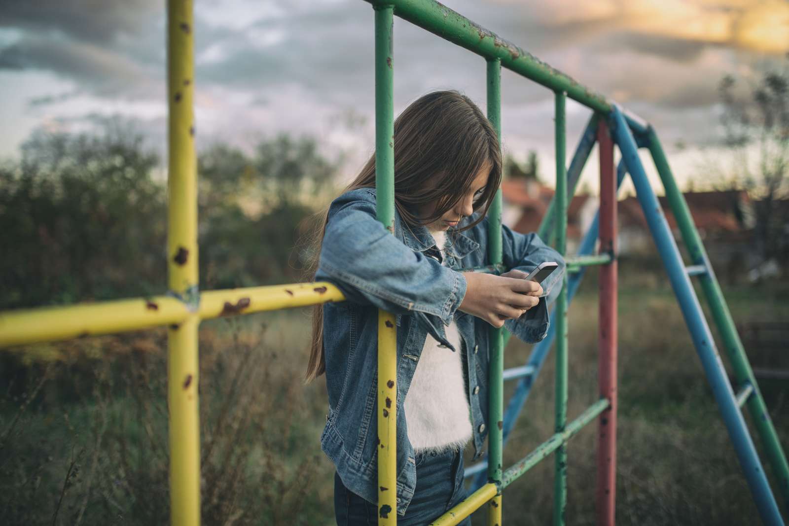 Pige står med armene igennem et klatrestativ og kigger op sin telefon