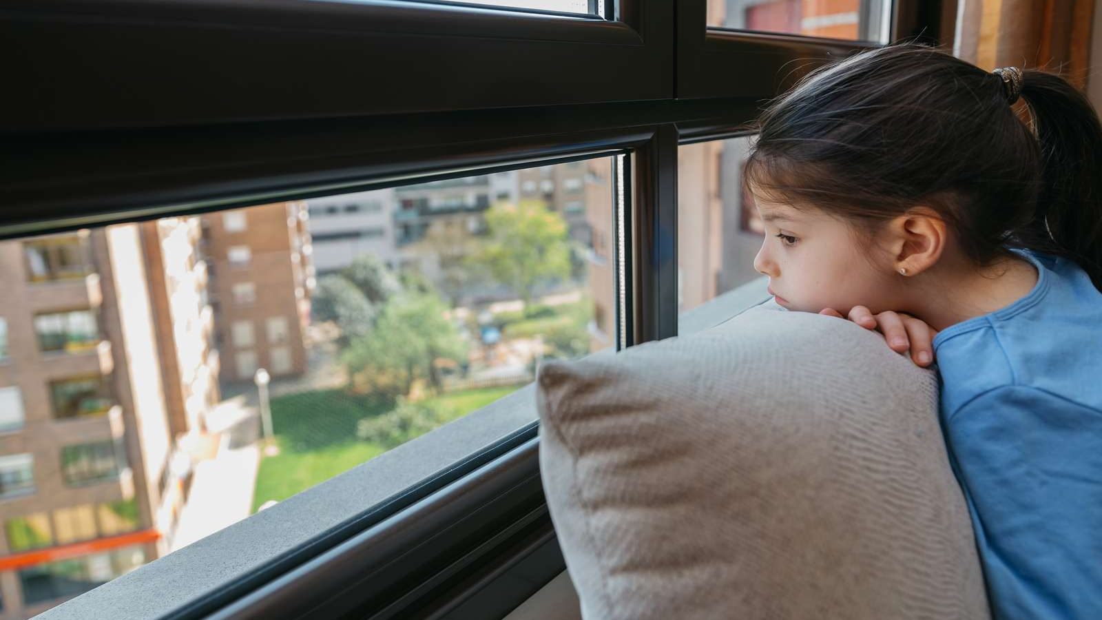 Mørkhåret pige med hovedet på en pude kigger ud af et vindue