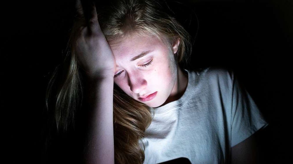 Trist pige holder hånden til hovedet mens hun kigger ned i sin mobil