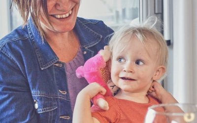 Lyshåret barn holder på en pink bamse, med en brunhåret kvinde i baggrunden