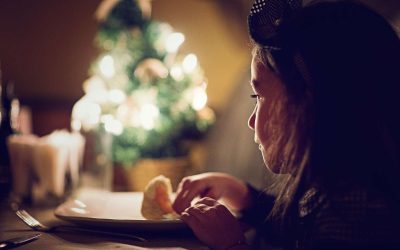 Mørkhåret pige sidder foran en tallerken, med et sløret juletræ i baggrunden.