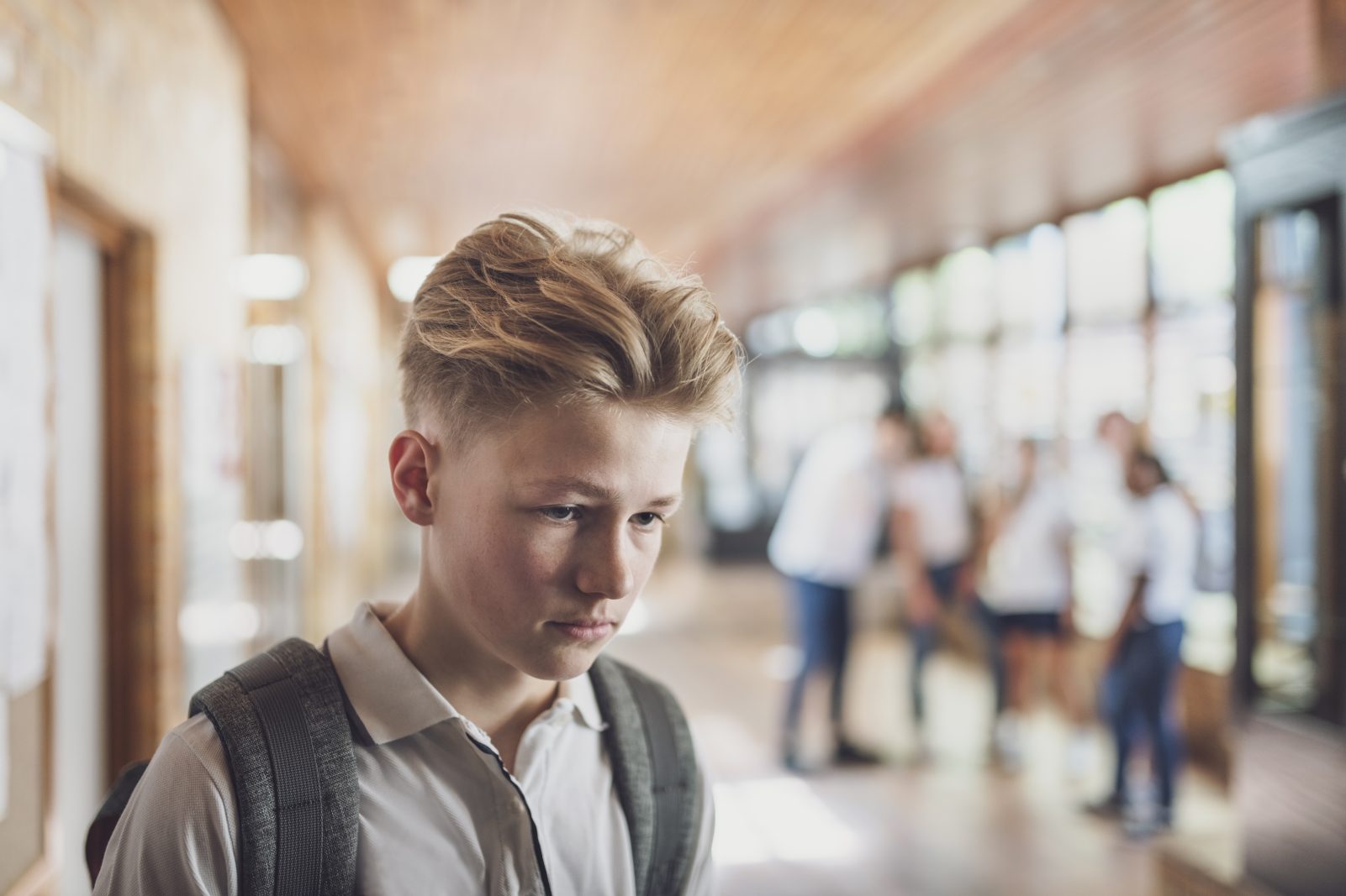 Blond dreng står i en gang, mens en gruppe andre unge står sløret i baggrunden