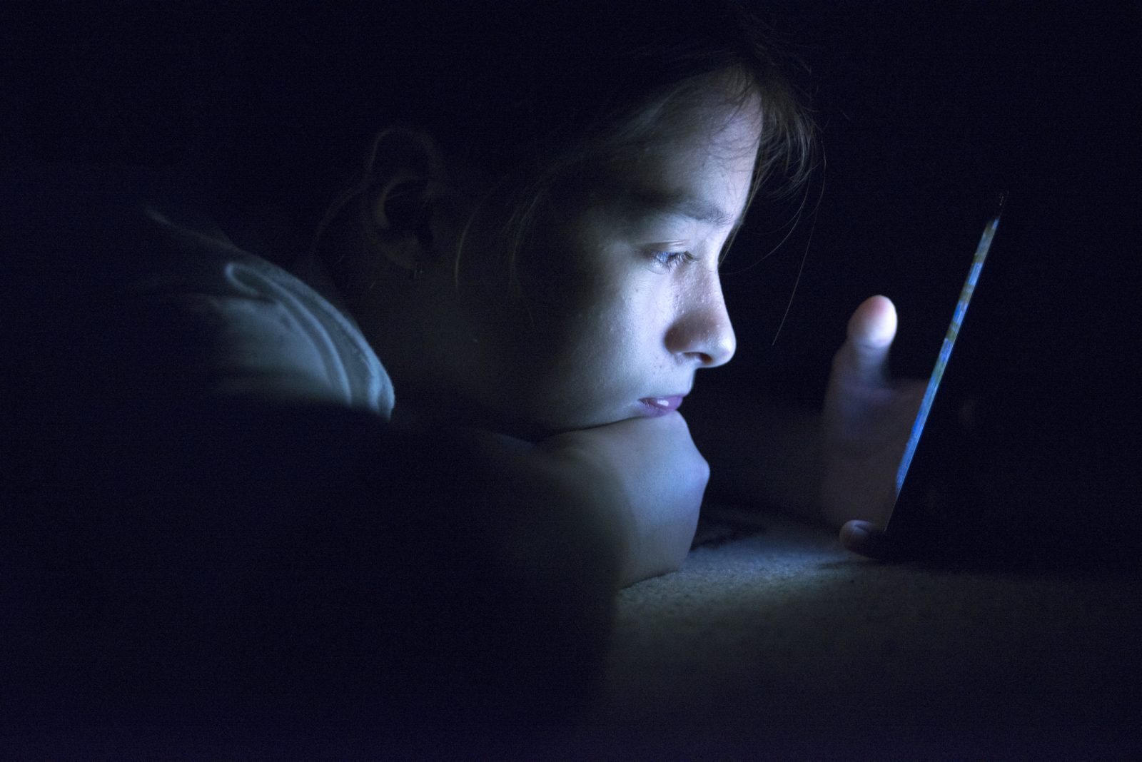 Pige ligger i mørke, oplyst af den telefon hun kigger på.