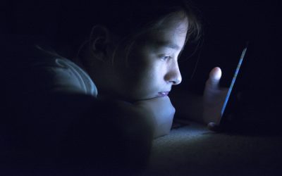 Pige ligger i mørke, oplyst af den telefon hun kigger på.