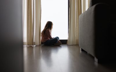 Pige sidder på gulvet og kigger ud af et vindue