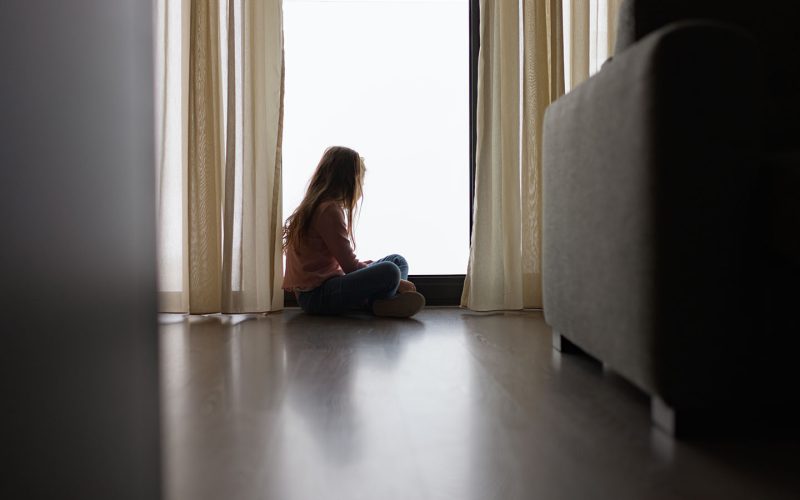 Pige sidder på gulvet og kigger ud af et vindue