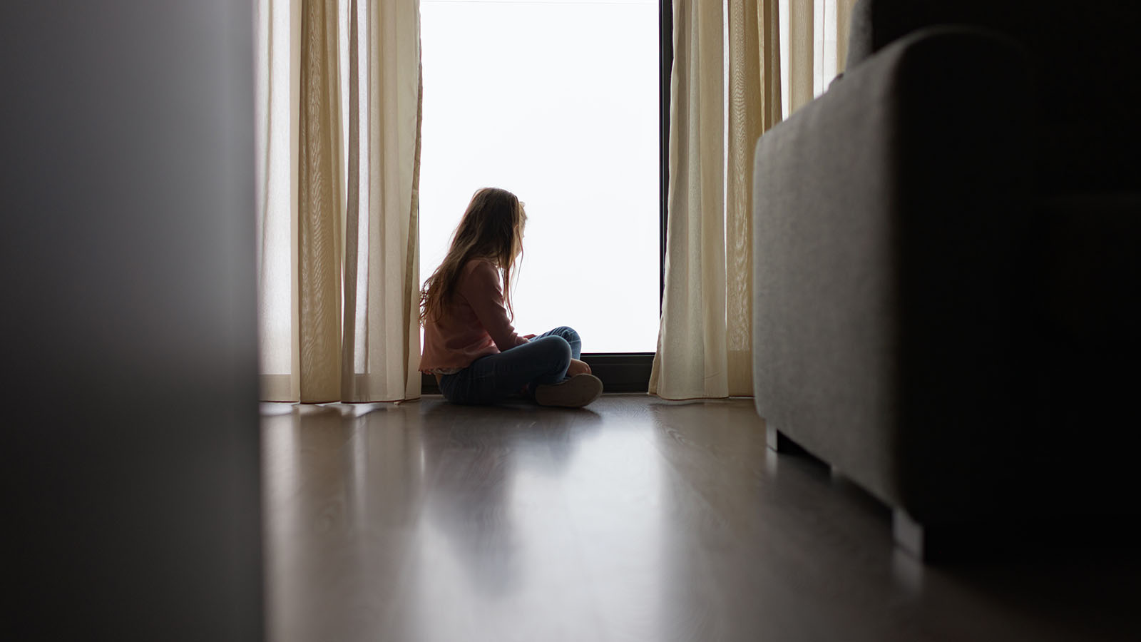 Pige sidder på gulvet og kigger ud af et vindue