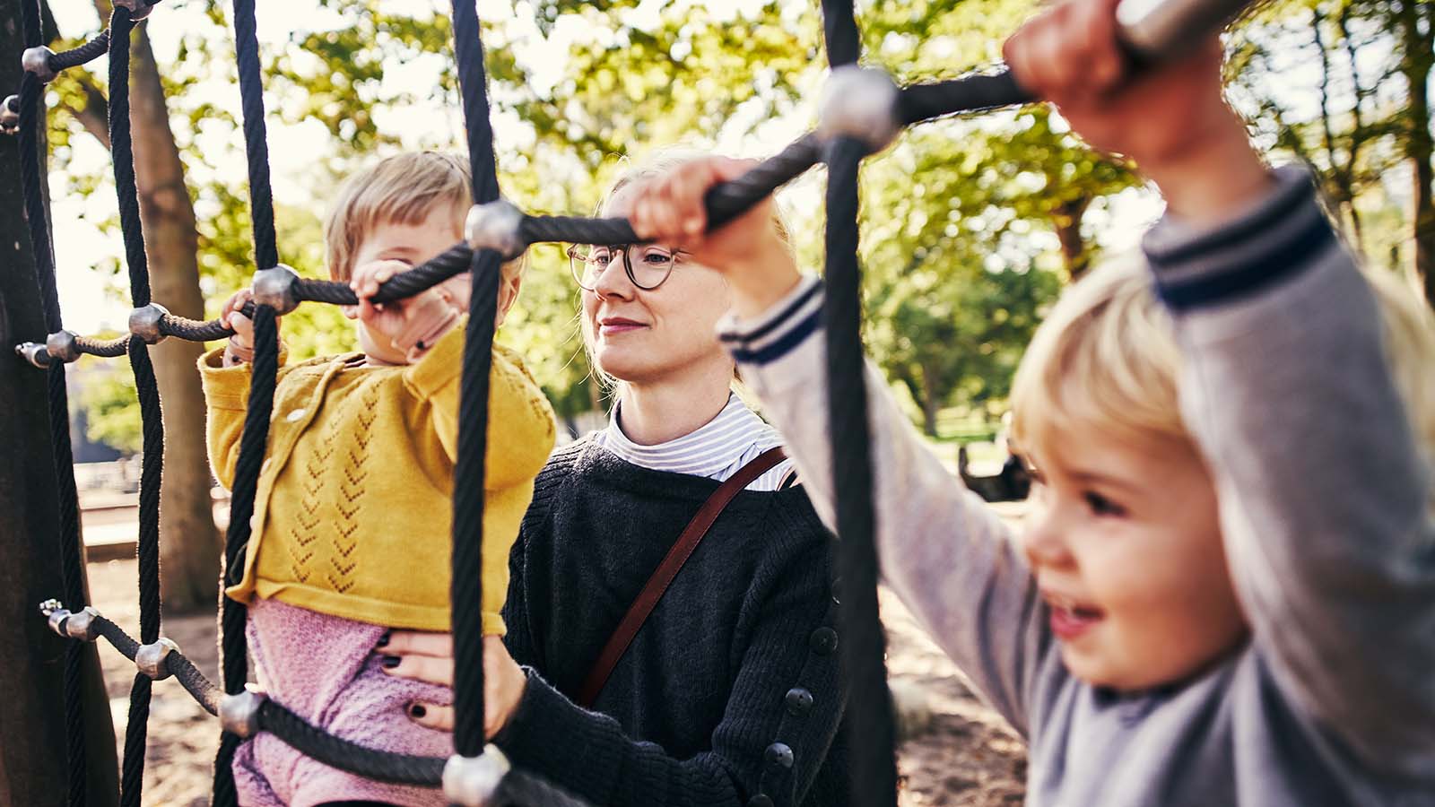 Lyshåret kvinde leger med to børn på et klatrestativ