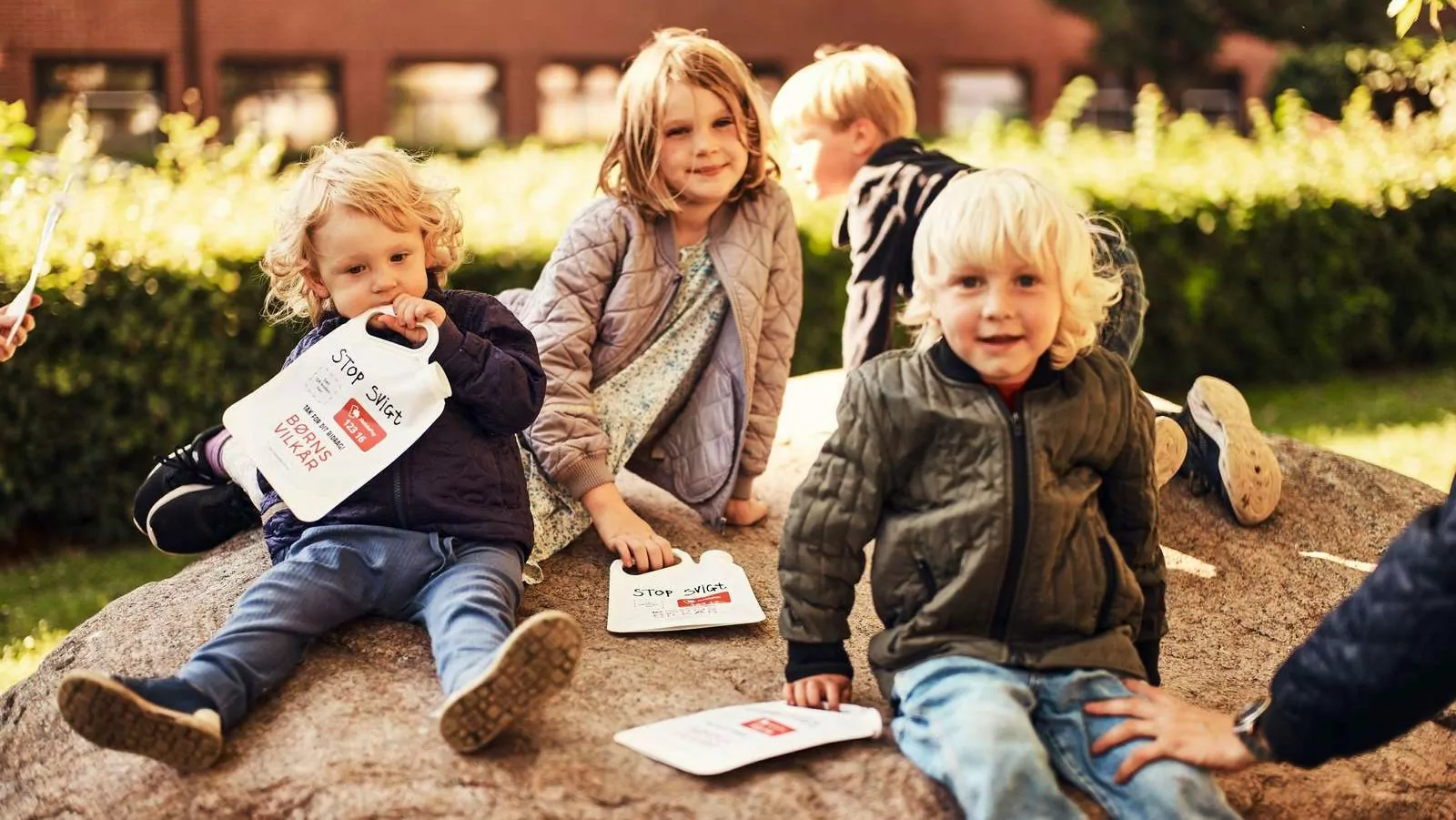 Fire små børn med indsamlingsbøtter sidder på en sten