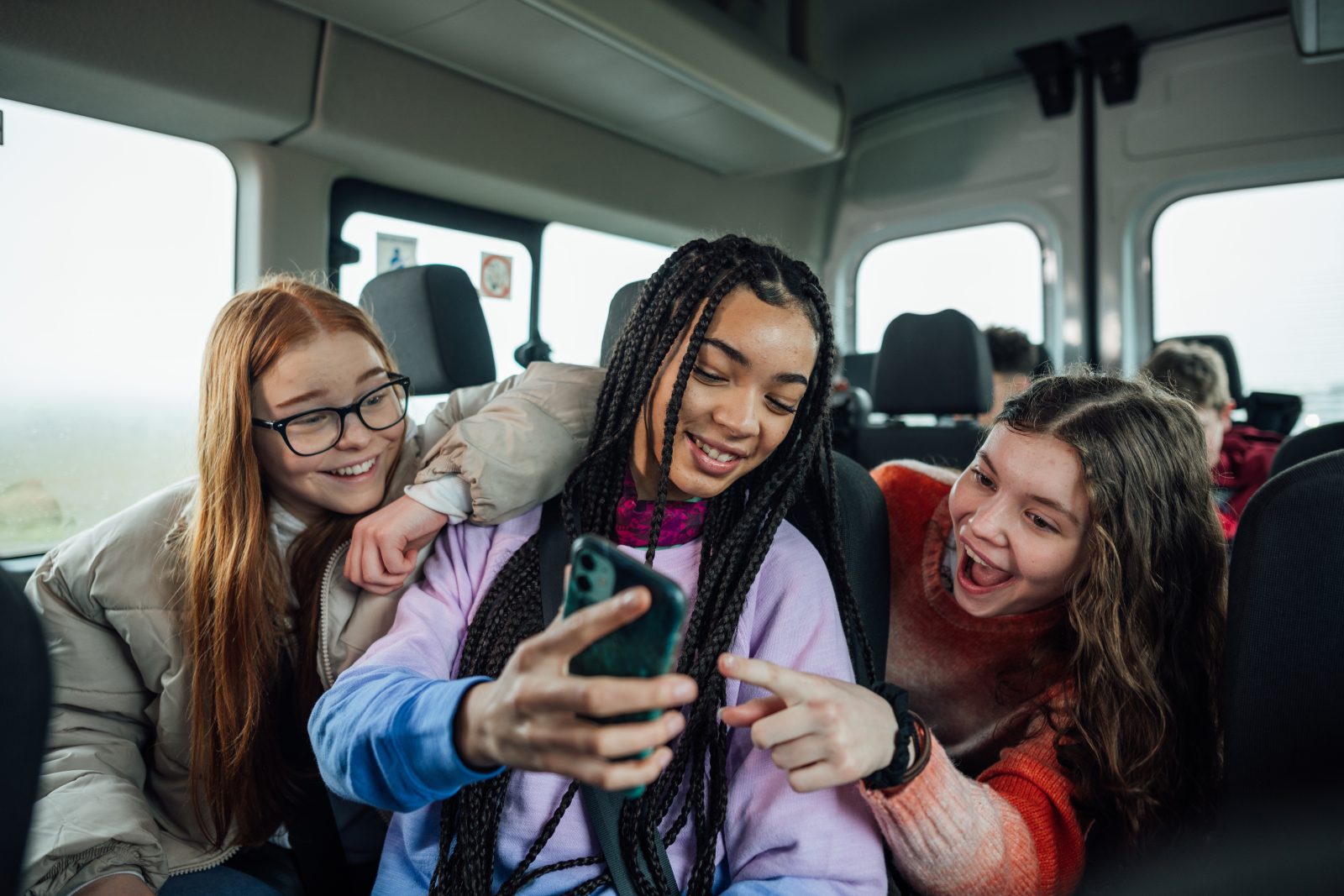 Tre piger sidder i en bus og kigger på en mobil
