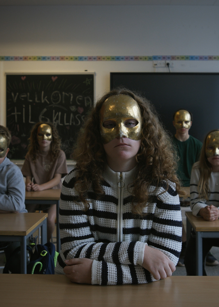 Pige med maske sidder i klasseværelse