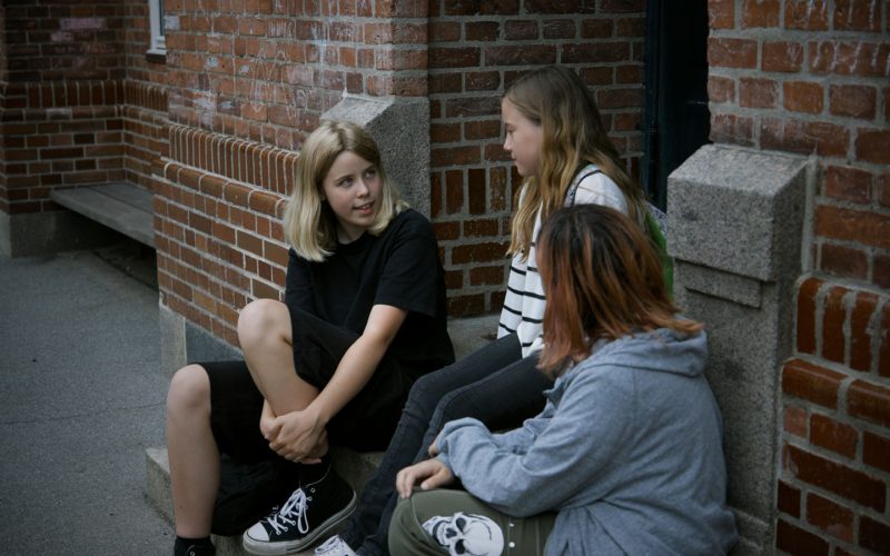 Tre piger sidder ved en indgang