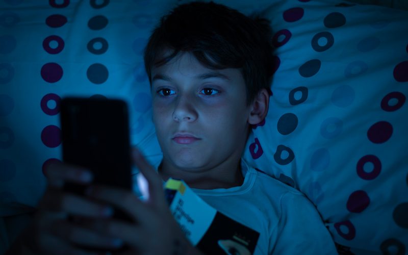 Dreng, der kigger på sin telefon i sengen
