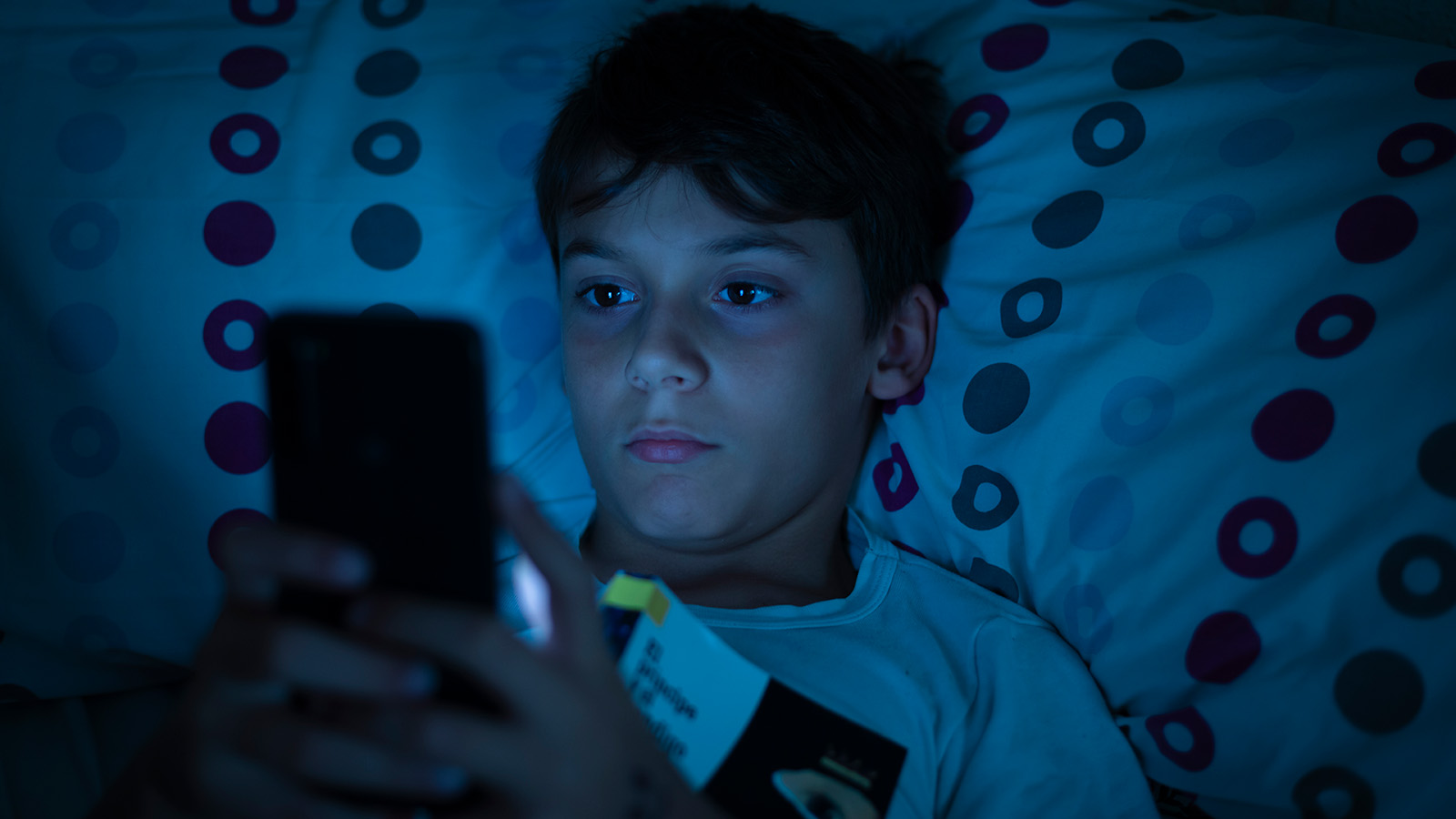 Dreng, der kigger på sin telefon i sengen