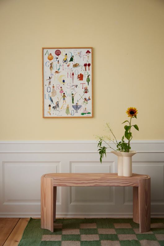 Plakat hænger på væg over et bord med en blomst på