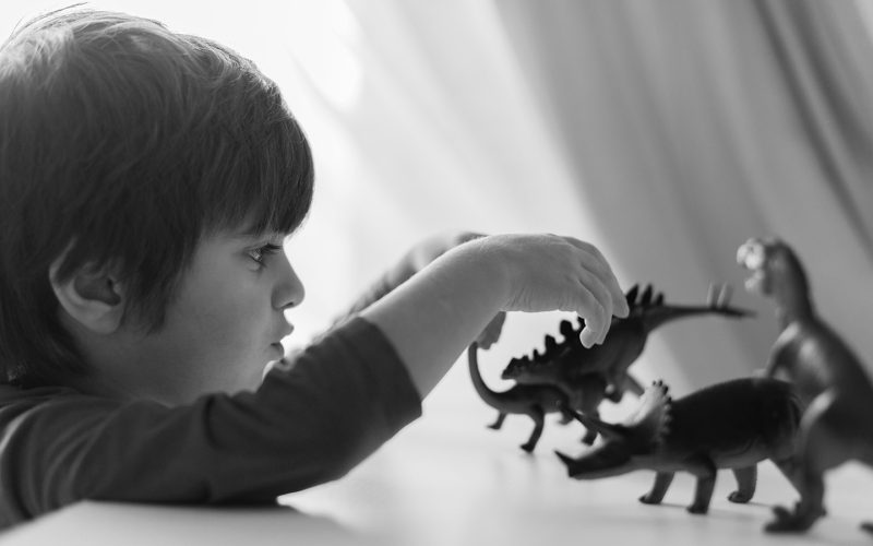 Sort-hvidt billede af dreng der leger med dinosaurer
