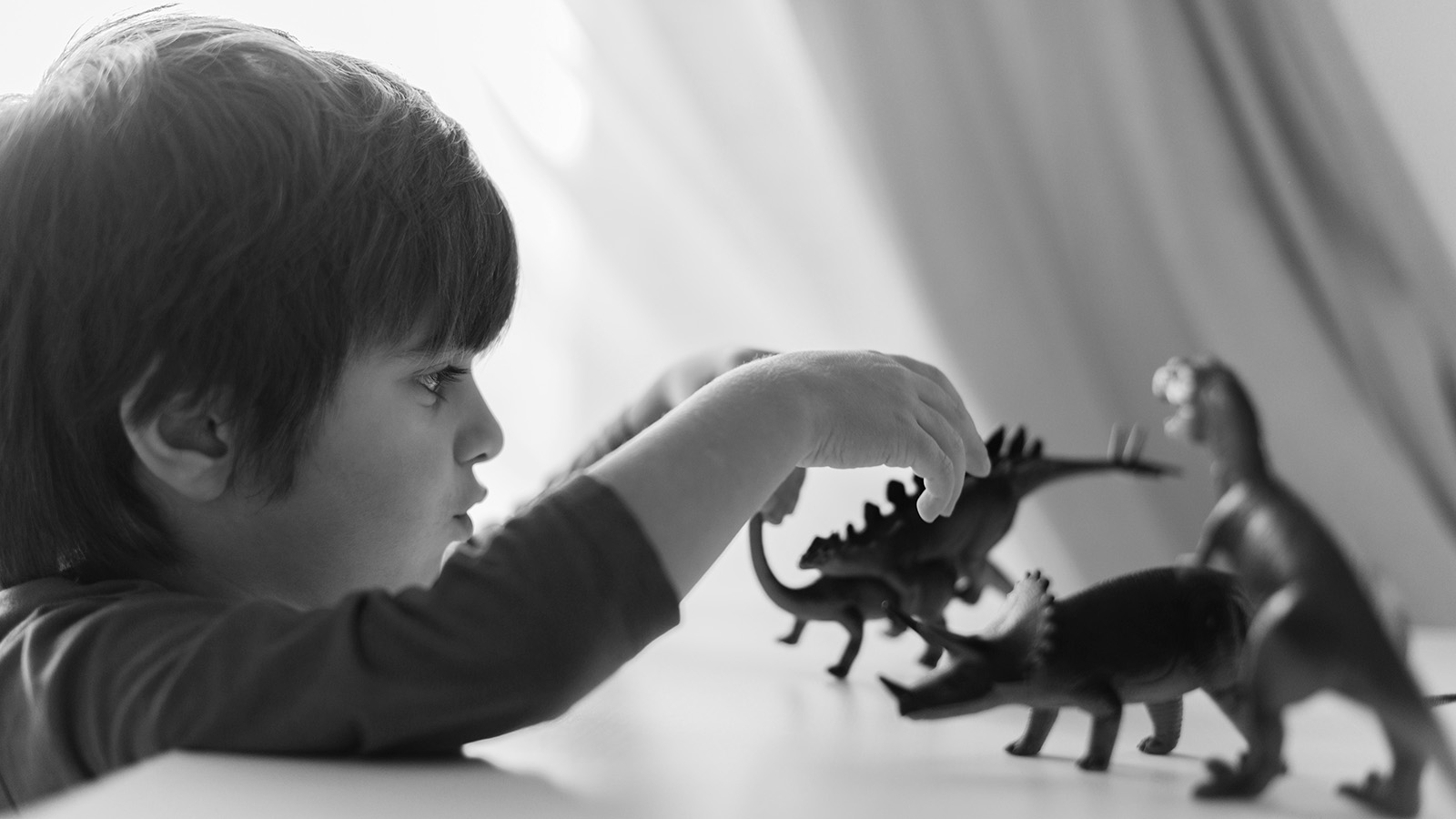 Sort-hvidt billede af dreng der leger med dinosaurer