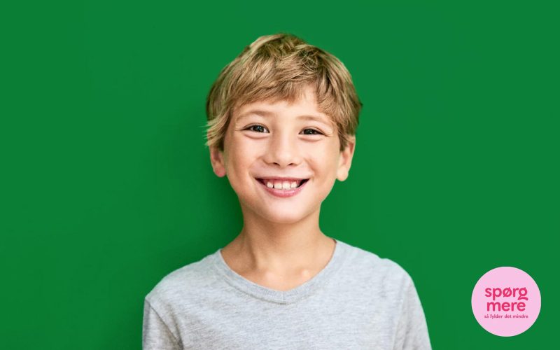Lyshåret dreng på grøn baggrund smiler til kameraet.