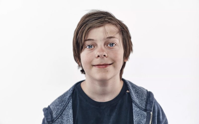 Brunhåret dreng på hvid baggrund kigger i kameraet